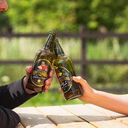 Two people sitting in a beer garden, clinking bottles of Kopparberg cider together in a Cheers motion.