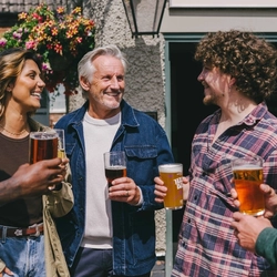 A mixed group of people stood outside a pub holding drinks.
