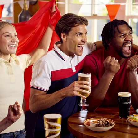 A group of friends sat round a table with drinks and small plates of food enjoying watching a sports event at a Flaming Grill venue.