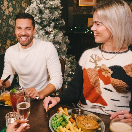 Four people sitting at a restaurant table with plates of food in front of them. One person is holding a glass of Level Head IPA, another person is holding a glass of champagne, and a cocktail and a glass of Guinness sit on the table.