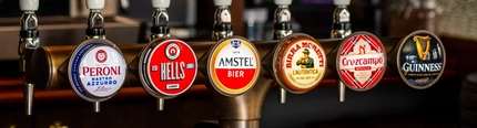 A close up view of a golden drinks tray and the beer taps for Peroni, Camden Hells, Amstel, Birra Moretti, Cruzcampo, and Guinness, on the bar at The London Apprentice.