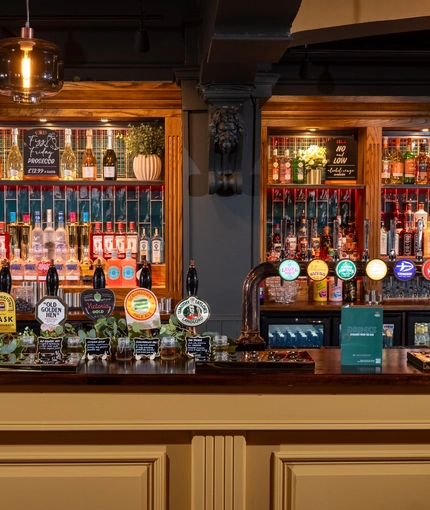 A close up view of the bar and beer taps at The Victoria in Lytham St Annes, with bottles of wine and alcoholic spirits on illuminated shelves behind the counter.