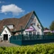 The exterior facade, signage, and seating area of the Rudds Arms in Marton-In-Cleveland; with an accessibility ramp leading up to the door; and picnic tables, shade umbrellas, and string lights on a raised deck area.
