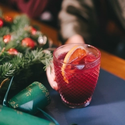 A hand resting on a festive decorated table is holding a cocktail type drink in a lowball glass.