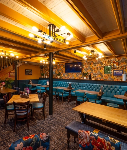 The interior restaurant seating area at the Old School House in Aberdeen, with a long, upholstered booth seat along one side of the room, a TV on the wall above it, and a wooden staircase leading to the upper floor.