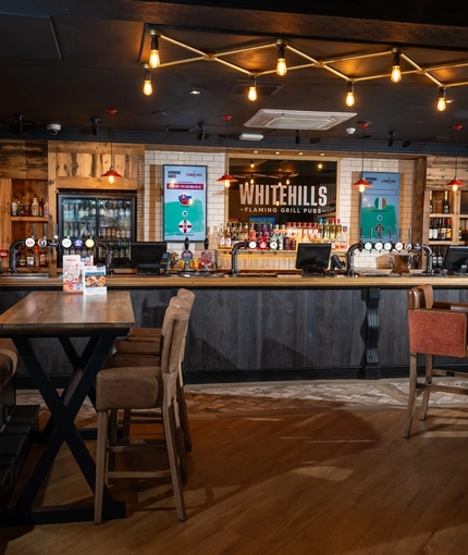 The bar and interior restaurant seating area at Whitehills, with TVs on the walls, and upholstered seats.