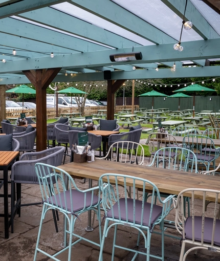 The exterior beer garden seating area at the Tredegar Arms in Bassaleg, with picnic tables and shade umbrellas on the lawn, an undercover area with a TV on the wall, and string lights hanging above all the tables. 