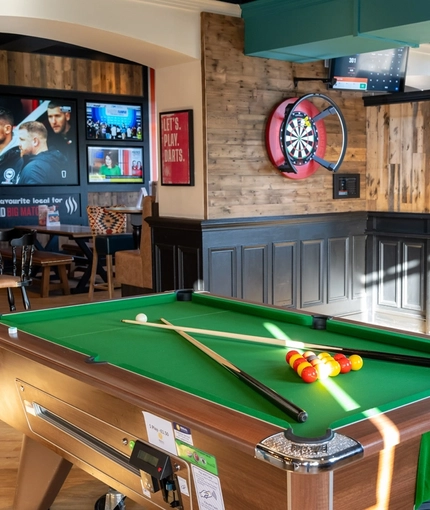 An interior restaurant seating area at Whitehills in Northampton, with TVs on the walls, a dartboard, and a pool table.