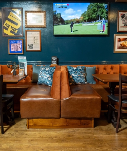 The interior restaurant seating area of the Cock & Pye, with upholstered booth seating and a TV on the wall.