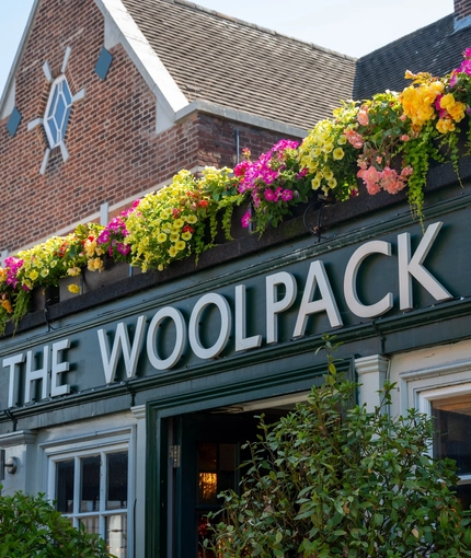 A close up view of the words "The Woolpack Inn" in white lettering on a dark green background, on the exterior wall of The Woolpack Inn in Norwich.