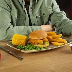 A children's Katsu Chicken burger at Hungry Horse venues, served on a plate with chips, corn on the cob, and peas. The plate sits on a wooden table next to a bottle of Fruit Shoot juice, cutlery, and a small pot of dipping sauce. 