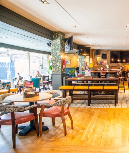 The bar and interior restaurant seating area of The Merlin, with wooden tables, upholstered seats, TVs on the walls, and pub game machines.