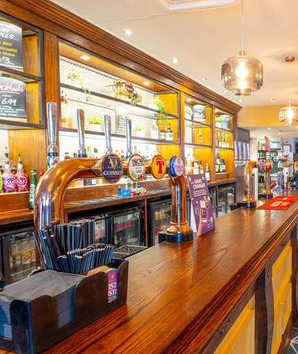 A close up view of the bar inside the Counting House in Dumbarton, with potted plants and bottles of alcoholic spirits on glass shelves behind the counter.