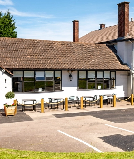 The exterior facade, signage, seating area, and car park of The Bramford Arms, with two potted topiary trees at one of the entrances.