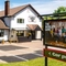 The exterior facade, signage, seating area, and car park of The Bramford Arms, with two potted topiary trees at one of the entrances.