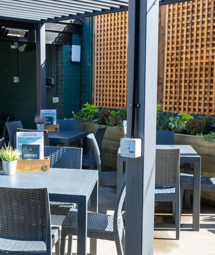 The exterior beer garden seating area of the Cock & Pye, with flowers and menus on each table and a TV on the wall.