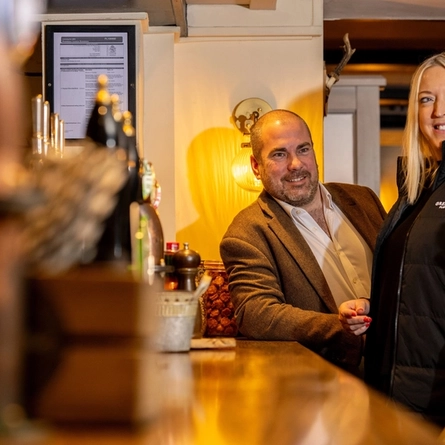 A Man and Woman stood in front of the bar, they are both smiling