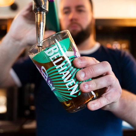 A lifestyle image showing a member of staff stood behind the interior bar pouring a pint of Belhaven Twisted Thistle.