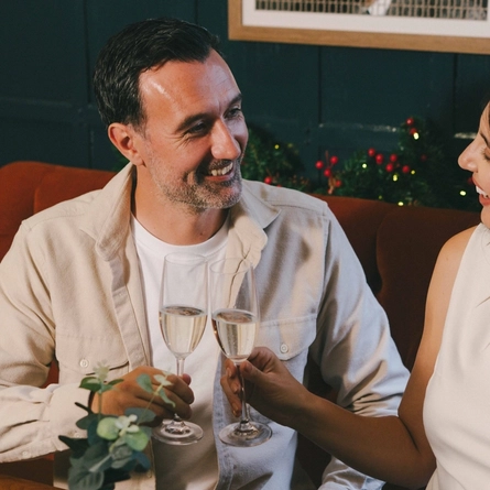 An image of 3 friends enjoying various side dishes and sparkling white wine while sat within the interior restaurant seating area.