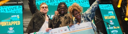 The winner of the Greene King Live At Your Local 2026 competition, Arjé Rayne, celebrating on stage with judges Danny Jones and Fleur East as they hold a giant cheque for the £10,000 prize.
