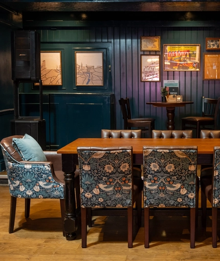 The wood panelled interior restaurant seating area of the Cock & Pye, with a large wooden dining table and upholstered seats.