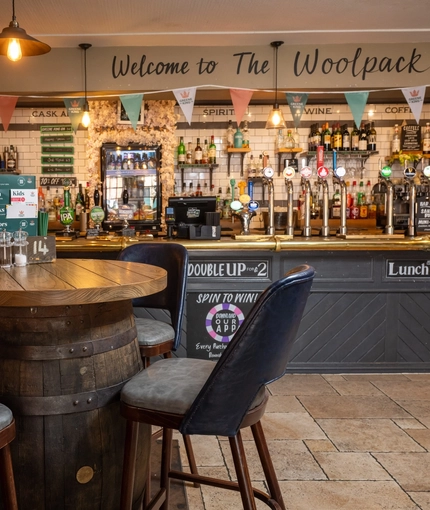 The bar area at The Woolpack Inn; with stone flooring, and four bar stools gathered around a restaurant table made from a beer barrel.