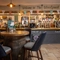 The bar area at The Woolpack Inn; with stone flooring, and four bar stools gathered around a restaurant table made from a beer barrel.