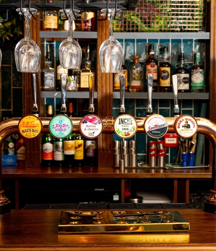 A close up view of a golden drinks tray and the beer taps for Hazy Day, Level Head, Old Mout Berries & Cherries, Inch's, San Miguel, and Birra Moretti; on the bar at The Talbot in Worcester.