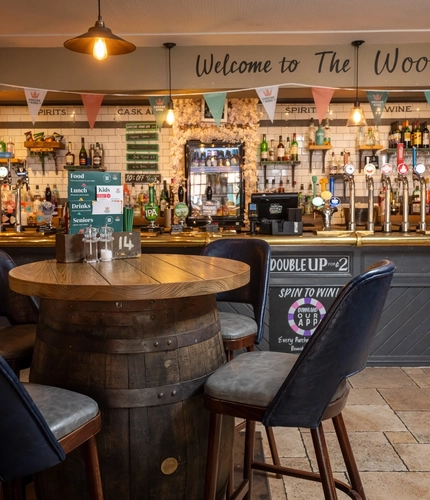 The bar area at The Woolpack Inn; with stone flooring, and four bar stools gathered around a restaurant table made from a beer barrel.