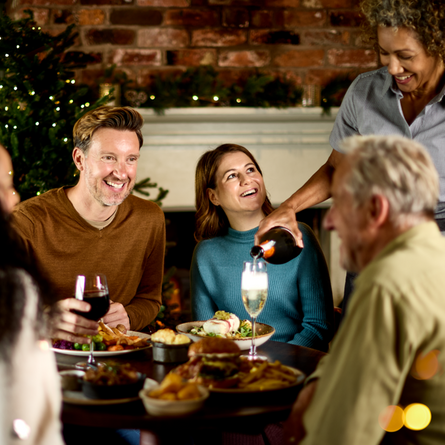 An image of 4 people sat around a table within the exterior restaurant and seating area with 1 person being served wine during a meal available at Chef & Brewer venues.