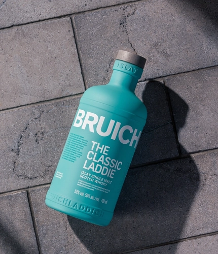 A bottle of Bruichladdich The Classic Laddie whisky, lying on a paved stone floor.