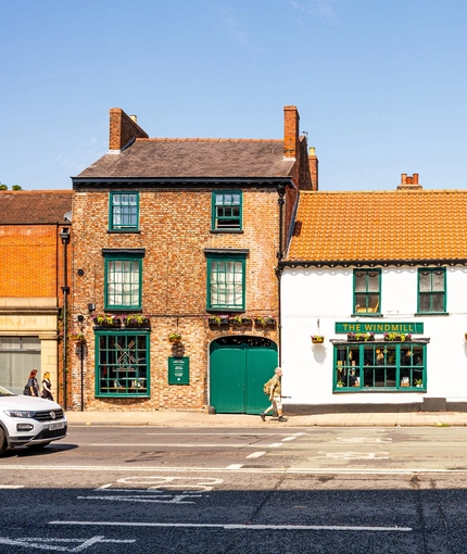 A view from across the road of the exterior facade and signage of The Windmill Inn in York, with flower baskets hanging on the wall.