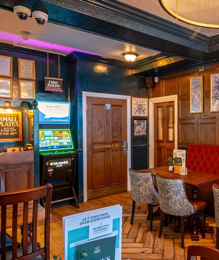 An interior restaurant seating area at The Earls Court Tavern, with a wood panelled wall, an upholstered booth seat, and a pub gaming machine.
