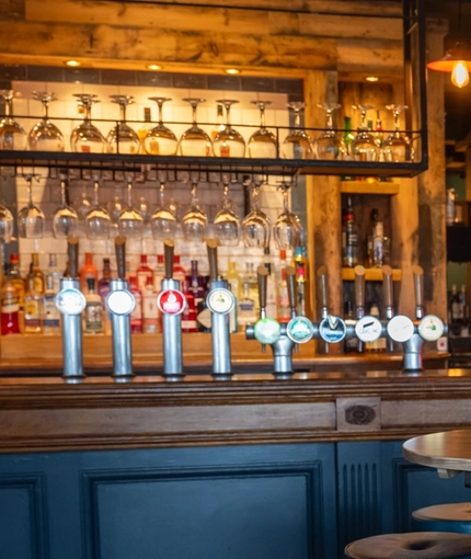 The bar and interior restaurant seating area at The Tamar, with upholstered bar stool seating, and a TV on the wall in the background.
