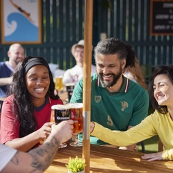 A mixed group of people seated at an outdoor table holding drinks.