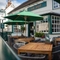 The exterior facade and seating area at the front of The Ship; with shade umbrellas on some of the wooden tables, and flower baskets hanging on the white walls of the pub.