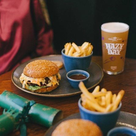 A person seated at a table with a plated burger and fries, in front of them.