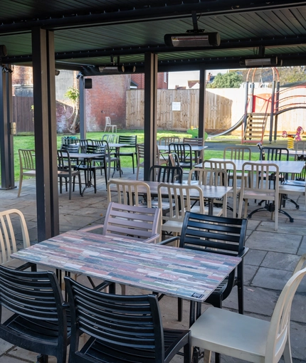 The exterior under cover beer garden seating area at the Green Posts in Portsmouth, with a TV, and a children's play area on the lawn next to it.