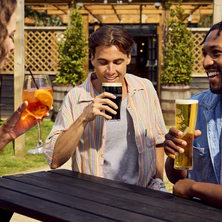 A group of friends all sat round a table holding drinks in the exterior beer garden at a Flaming Grill venue.