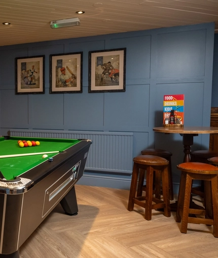 The interior games area at The Heron in Havant; with a pool table, a TV on the exposed brick wall, and a restaurant table with bar stool seating.