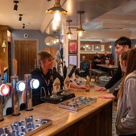 A member of staff serving two guests at the bar inside the Weathervane.