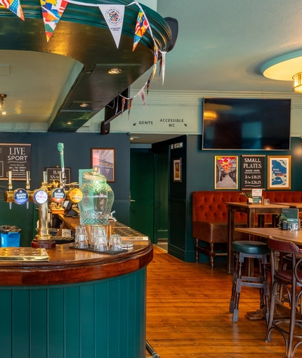 A close up view of the bar and interior restaurant seating area at the Royal George; with golden drinks trays on the counter, and a TV on the wall.