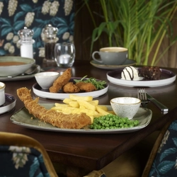 A wooden indoor table holding a plate of Fish & Chips, with other plated meals and drinks.
