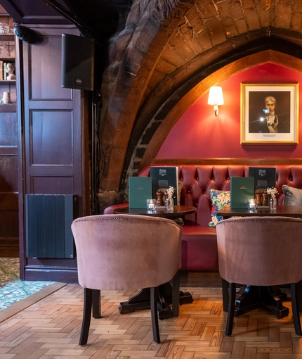 An image focusing on one of the interior restaurant seating area tables situated within a gothic stone arch with chairs, cushioned seating and wooden flooring at The Watergates Bar.
