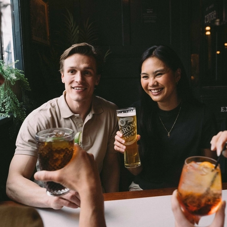 A group of friends sat around a table in the seating area of a Greene King venue enjoying drinks on a £3 deal.