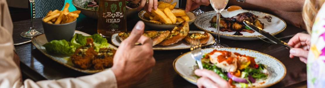 Lots of food on a table with drinks and people sat around