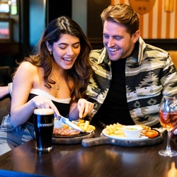 A man and woman sitting together at a table with drinks and plates of food in front of them.