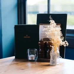 A close up view of menus, salt and pepper mills, a tea light, and a table ornament, on a restaurant table inside Ye Olde Swan.