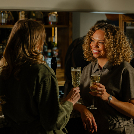 An image of 2 customers enjoying glasses of Prosecco stood within the interior bar area at The Crown.