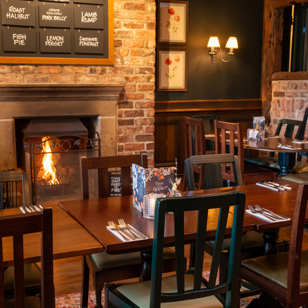 An interior restaurant seating area at The Blue Cap, with wooden tables and chairs, and a large brick fireplace.